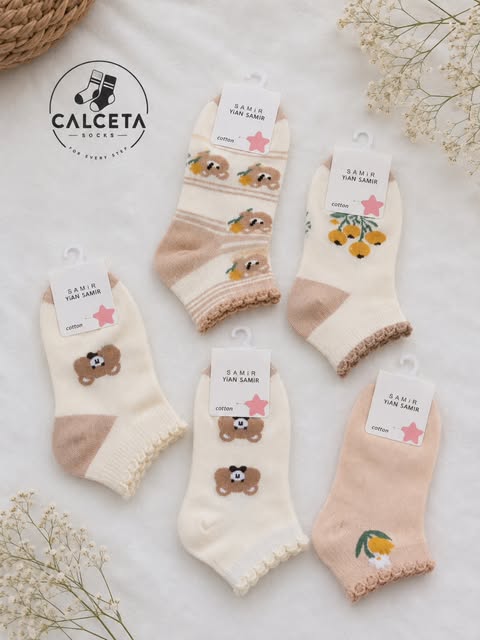 Lot de cinq chaussettes enfant en coton, tons crème et beige, motifs oursons et fleurs, présentées à plat sur du lin clair.